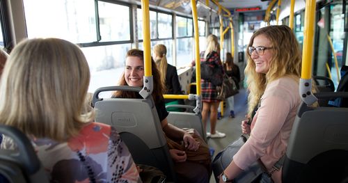 Sister missionaries ride bus in Latvia while conversing with others.