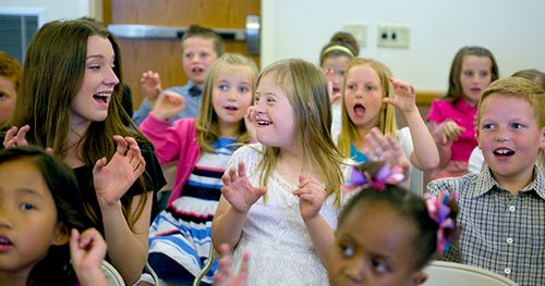 Primary-age children sing while making hand gestures.