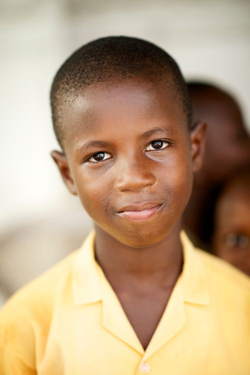 A portrait of a young boy in Ghana wearing a yellow button-up shirt.