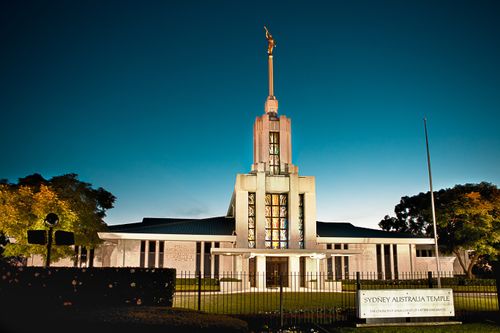 A view from the front of the Sydney Australia Temple in the low light of the evening, including the name sign on the black gate.