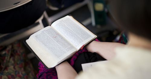 A Korean woman sitting and holding an open book of scriptures at Church.