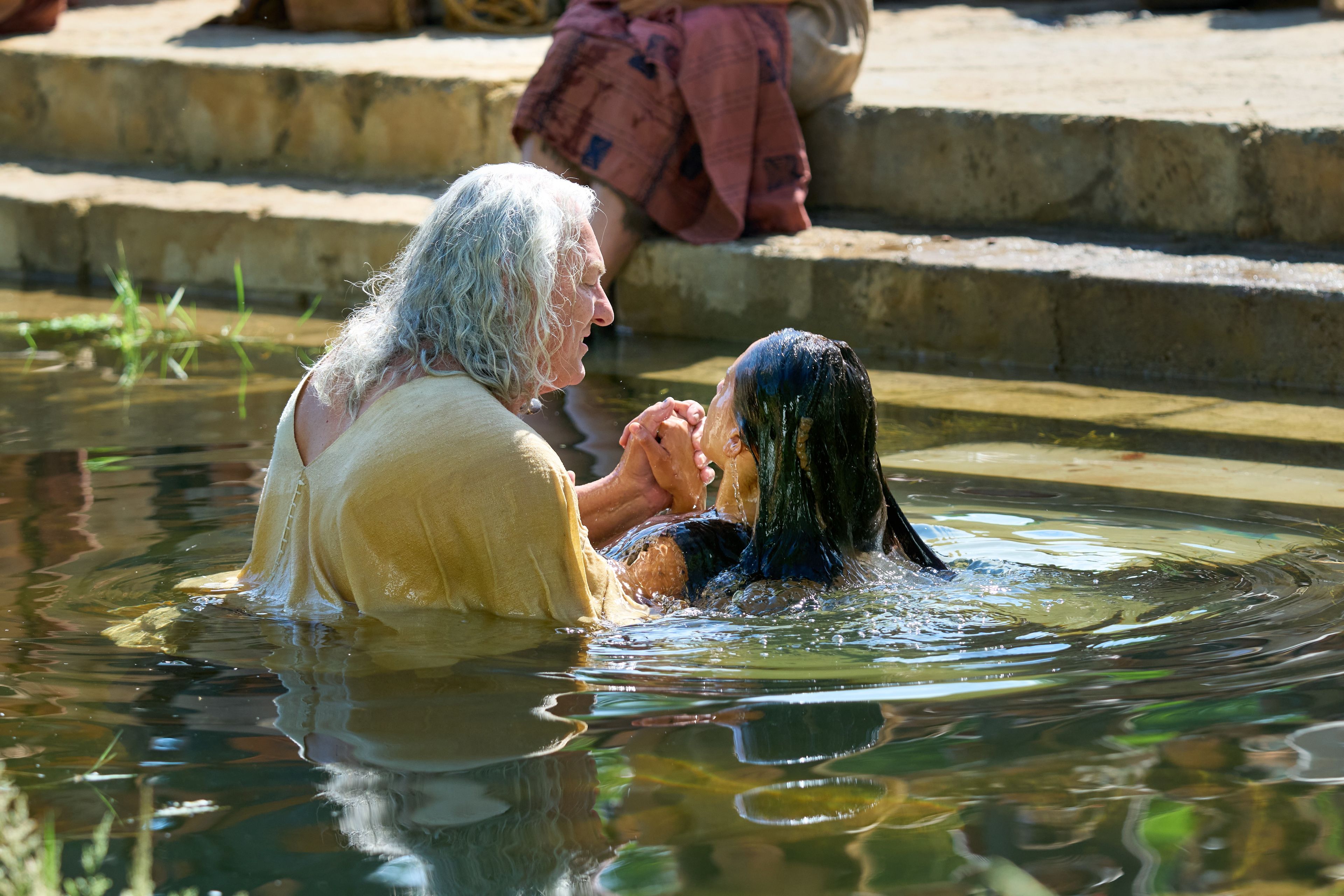 Nephi baptizes a woman in a pool of water. He had previously been set apart and given the authority by the resurrected Savior, Jesus Christ.