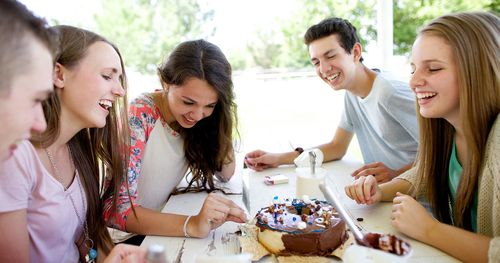 Young men and women sit together decorating a cake and laughing and having fun.