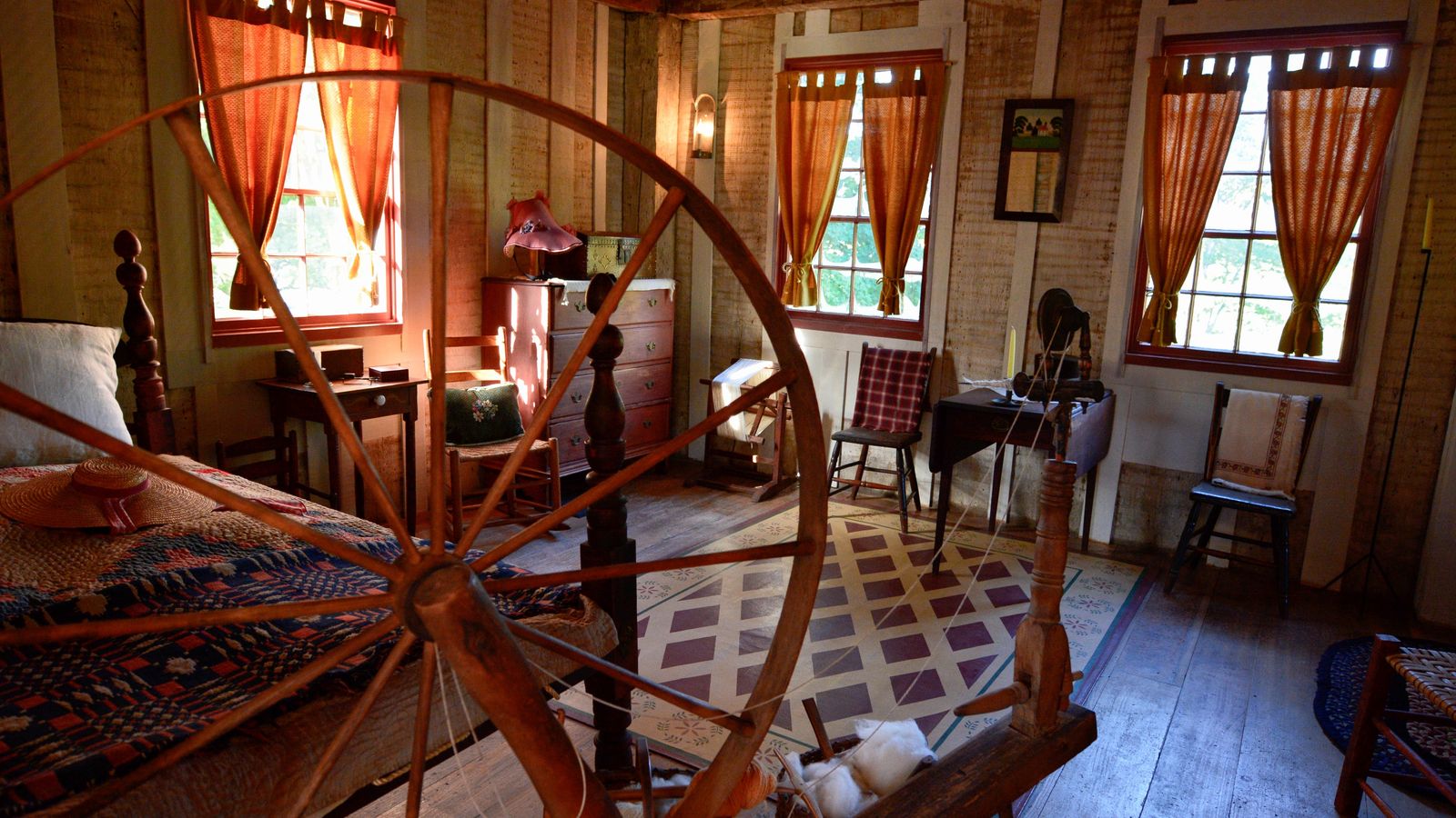 A large spinning wheel, a bed, a dresser, and several chairs in the house on the Smith family farm.