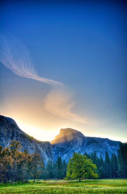 The sun rising over the Half Dome mountain in Yosemite National Park with trees below.
