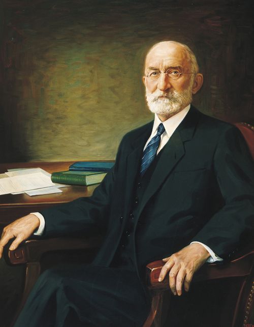 A portrait by C. J. Fox of President Heber J. Grant in a black suit and blue tie sitting in a chair.