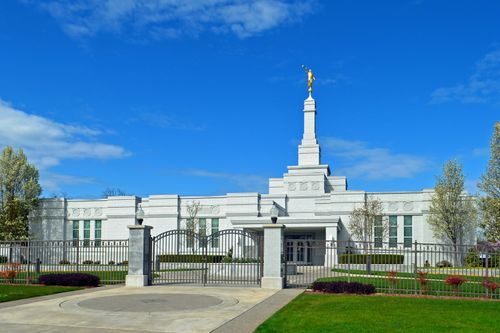 The front entrance to the Medford Oregon Temple, surrounded by a fence, with a blue sky above.