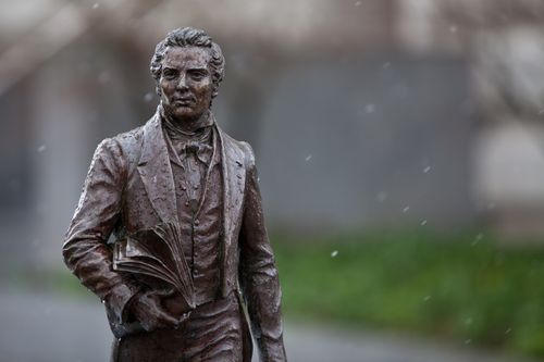 A small bronze statue of Joseph Smith seen outside on Temple Square on a snowy day.