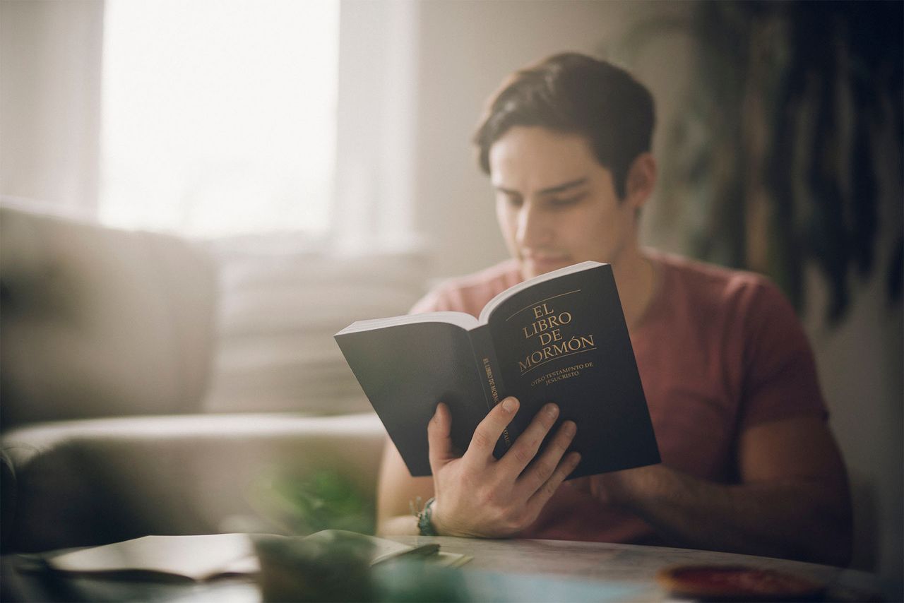 Un hombre joven estudia el Libro de Mormon en la sala de su casa