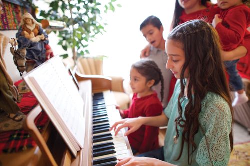 A girl plays the piano while her family stands and sings.