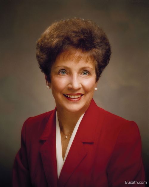A photograph of Dwan Jacobsen Young sitting against a dark gray background, wearing a red blazer with a white blouse.