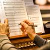 Two hands make notations on printed sheet music at an organ.