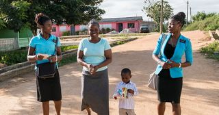 Zwei fröhliche Missionarinnen, die mit einer Frau und einem Kind sprechen