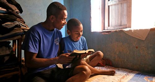 A father reads the scriptures with his son.