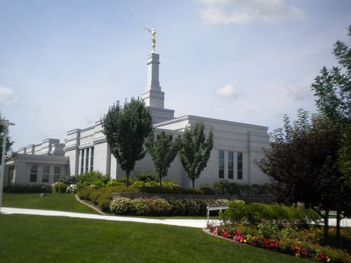 An angled view of the Palmyra New York Temple, with green trees and colorful flowers growing on the grounds.