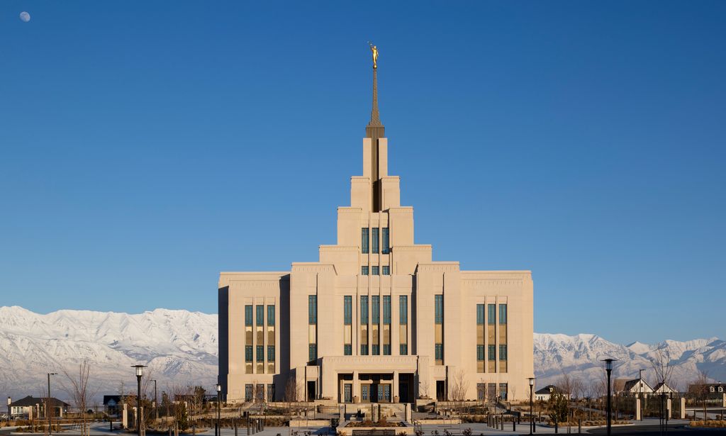 Exterior image of the Saratoga Springs Utah Temple taken during the day. There are mountains with snow are in the background.