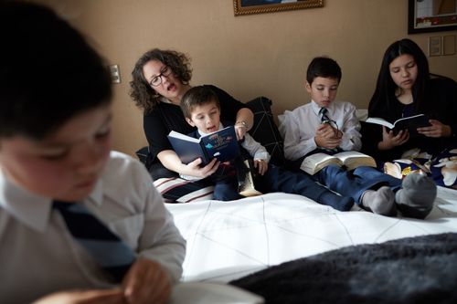 A mom sitting on a bed with her three sons and one daughter, reading the scriptures together.