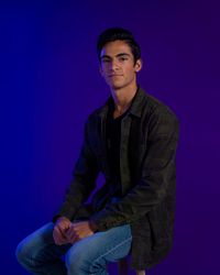 Larkin, a young man sits on a blue-purple background and looks to camera.